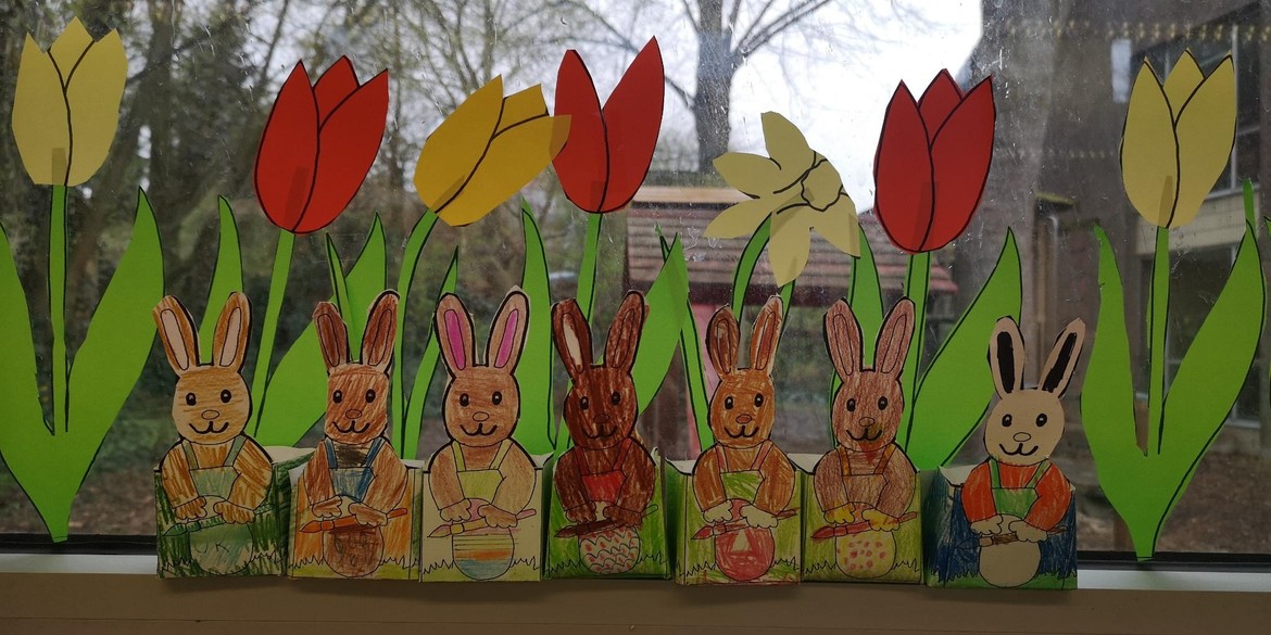 An einem Fenster kleben gebastelte Osterhasen und Tulpen.