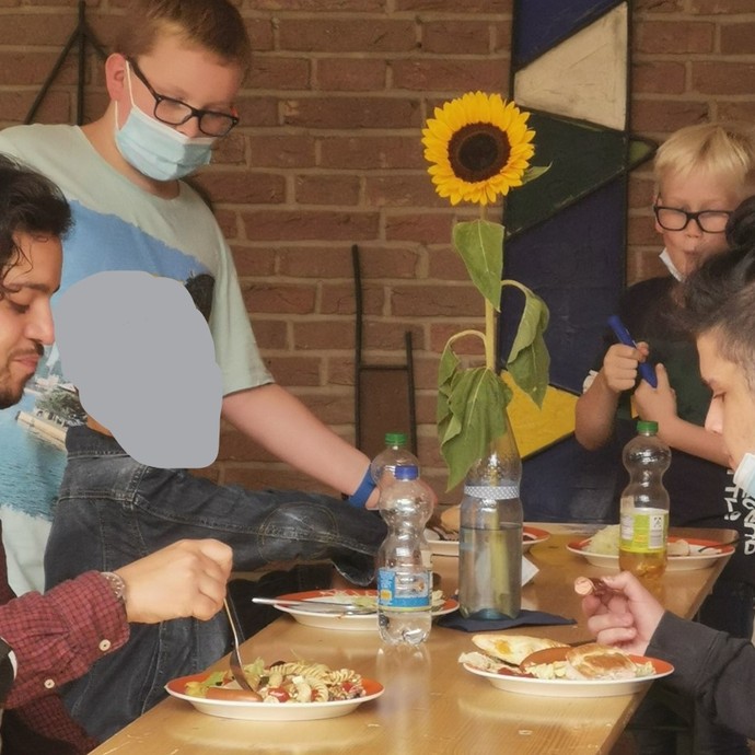 Ein Mann und drei Jugendliche sind um eine Bierbank versammelt und essen Nudelsalat. (vergrößerte Bildansicht wird geöffnet)