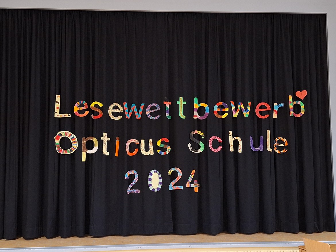 Vor einem schwarzen Vorhang hängen bunte Buchstaben.