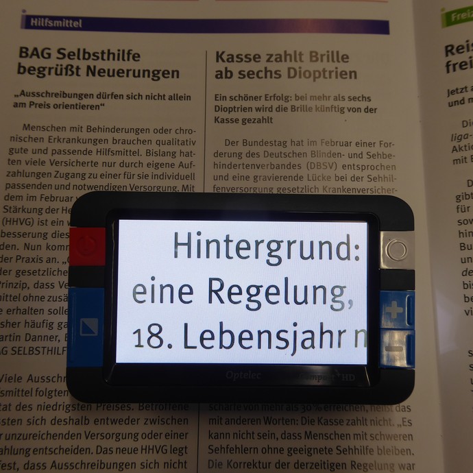 Das Bild zeigt ein Buch mit einer elektronischen Lupe. (vergrößerte Bildansicht wird geöffnet)