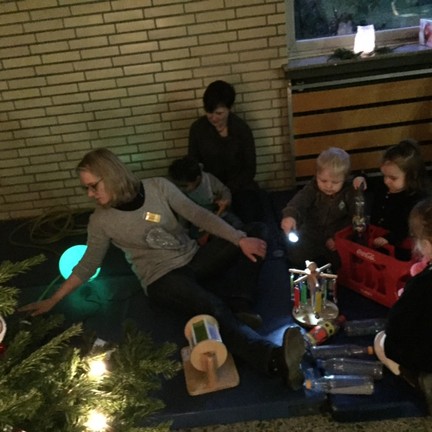 Eltern, Kinder und Frühförderinnen sitzen auf Matten und spielen mit Geräten.