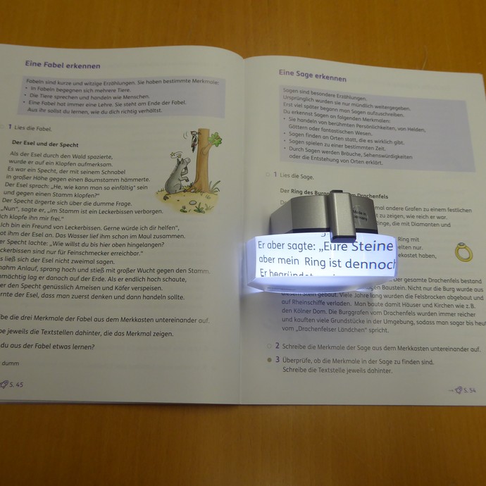 Das Bild zeigt ein Lesebuch mit einer elektronischen Lupe. (vergrößerte Bildansicht wird geöffnet)