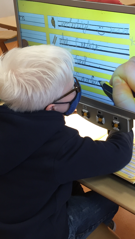 Ein Junge schreibt am Bildschirmlesegerät Wörter in Schreibschrift zu kleinen Bildern von Gegenständen.