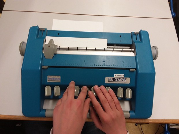 Es ist eine Schreibmaschine des Fabrikats Eurotype zu sehen. Ein Blatt ist eingespannt, ein*e Punktschriftschreiberin tippt. Es ist eine Schreibmaschine des Fabrikats Eurotype zu sehen. Ein Blatt ist eingespannt, ein*e Punktschriftschreiberin tippt.