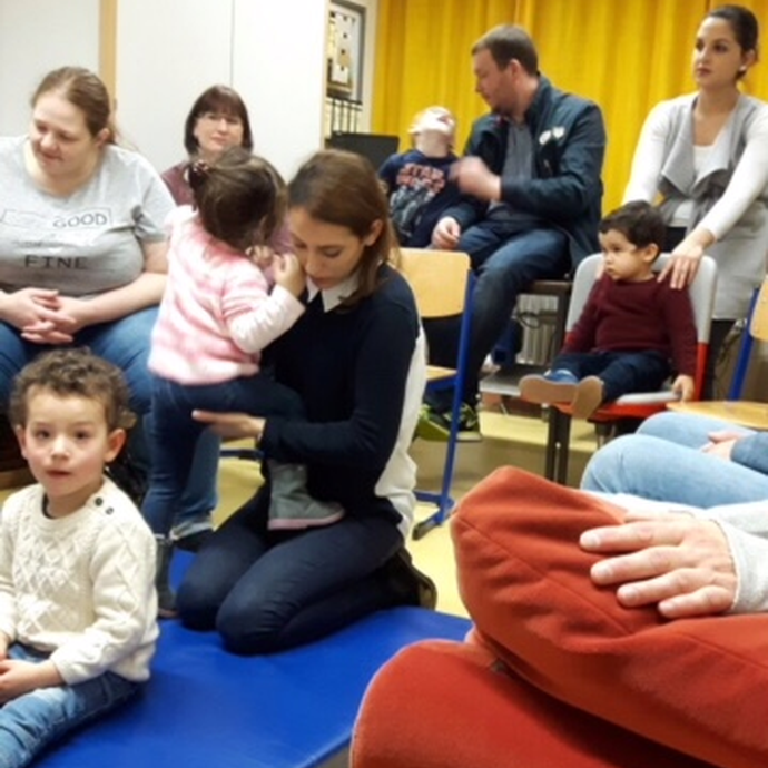 Kinder und Eltern sitzen auf dem Boden eines Klassenzimmers und lauschen. (vergrößerte Bildansicht wird geöffnet)