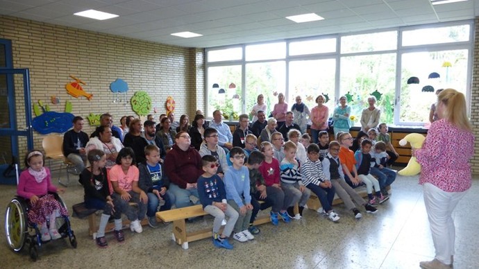 Kinder und Eltern sitzen auf Bänken im Foyer der Opticus Schule.
