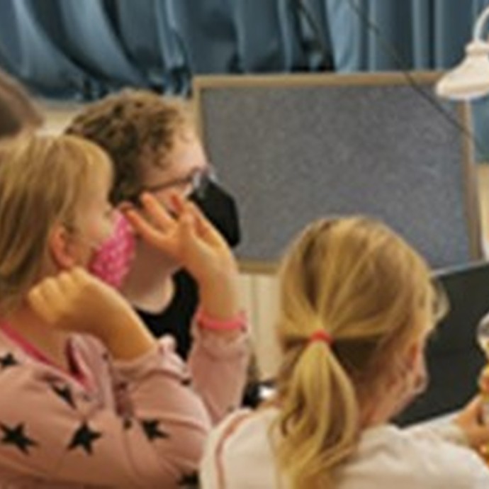 Drei Kinder und eine Frau lauschen. Alle tragen eine Maske. (vergrößerte Bildansicht wird geöffnet)