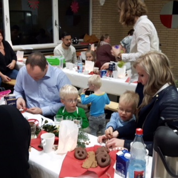 Kinder und Eltern sitzen auf Tischen im Foyer der Opticus Schule. (vergrößerte Bildansicht wird geöffnet)